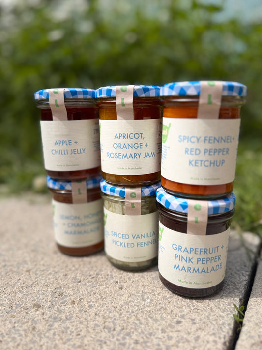 Five jars of different jams and ketchups with labels on a concrete surface. Advertising Fizzel Giftcards, the perfect gift for your foodie friends